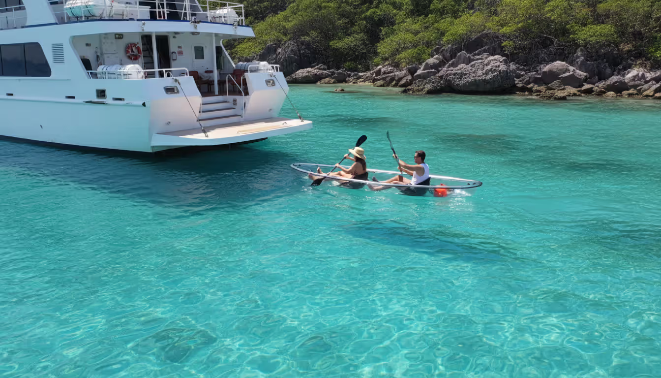 Couple kayaking in turquoise water near a luxury cruise ship stern marina platform with tropical rocky coastline in background