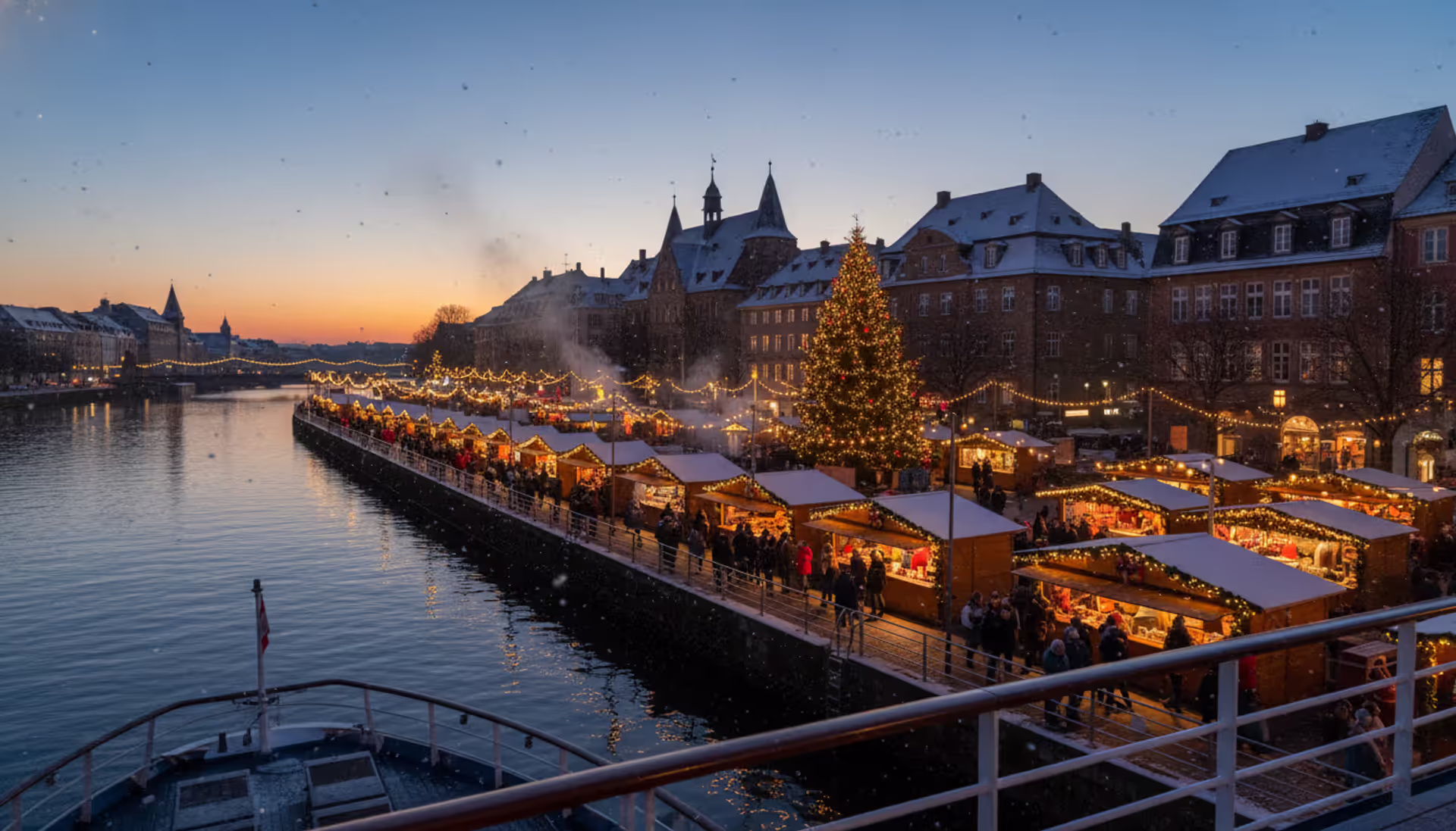 Evening view from a river cruise ship deck overlooking a European Christmas market on the riverbank with warm lights and light snowfall
