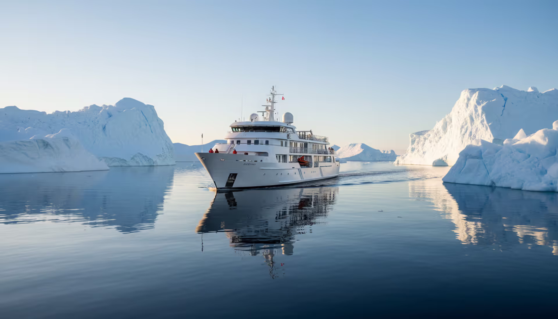 Luxury expedition cruise ship sailing among large blue icebergs in calm Antarctic waters under clear sky