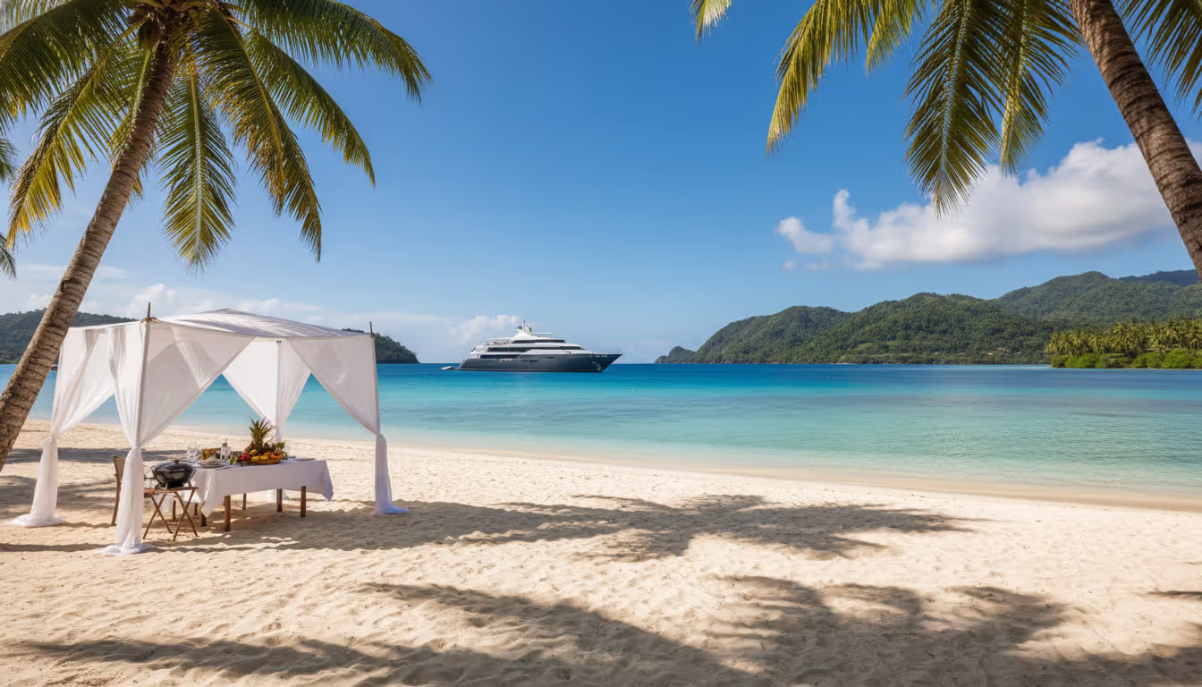 Tropical Fiji beach with white sand, turquoise water, a small luxury expedition cruise ship anchored in the bay, and an elegant beach barbecue setup under a white canopy
