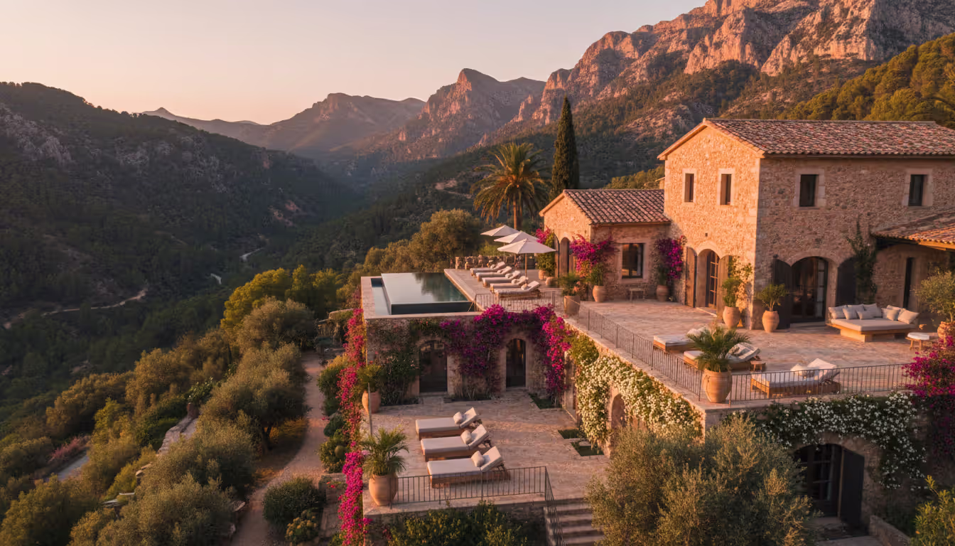 A converted stone finca spa retreat in Mallorca with Tramuntana mountain landscape, terrace loungers, and Mediterranean gardens at sunset