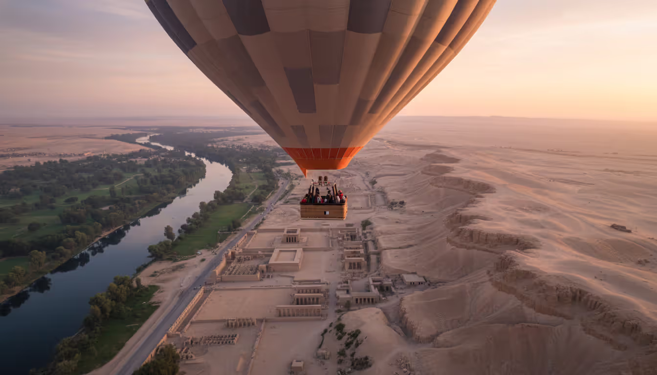 Hot air balloon flying over Luxor West Bank at sunrise with Nile valley temples and desert hills below
