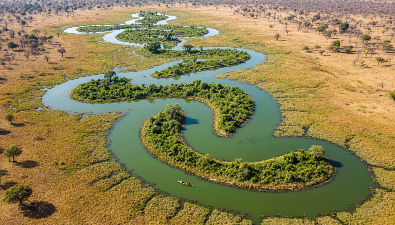 Aerial view of the Okavango Delta showing winding turquoise water channels through green islands with a traditional mokoro canoe
