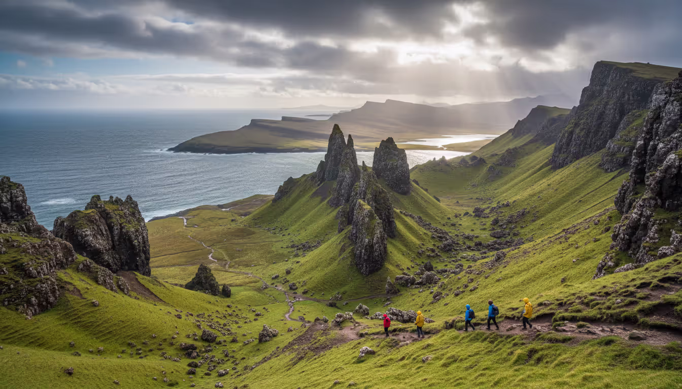 Dramatic Quiraing landscape on the Isle of Skye with steep green slopes, rocky peaks, coastal views, and a few hikers walking along a trail under partly cloudy sky