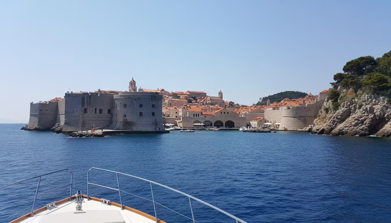 View from a yacht bow approaching Dubrovnik old town with its iconic stone walls and terracotta rooftops from the sea