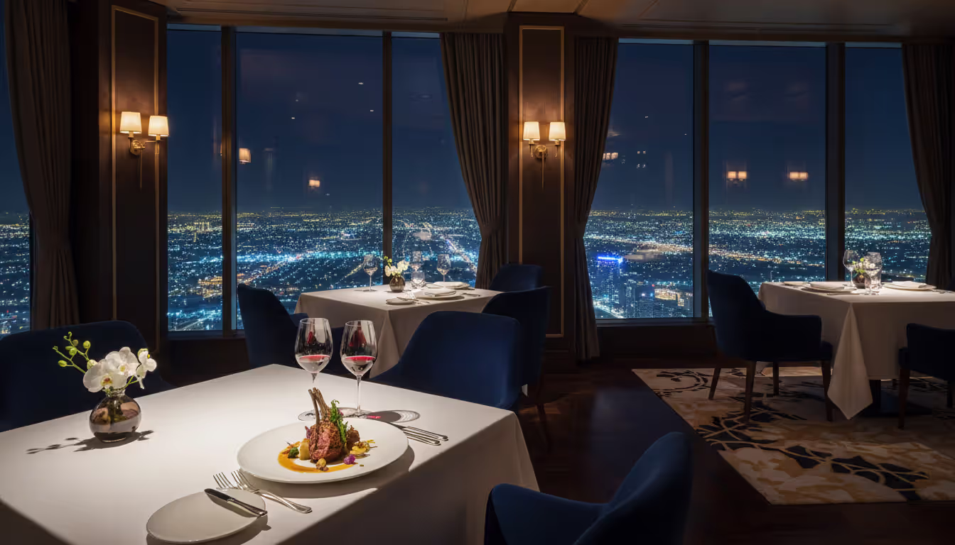 Upscale high-rise restaurant interior with floor-to-ceiling windows showing Dubai city lights at night and elegant table setting