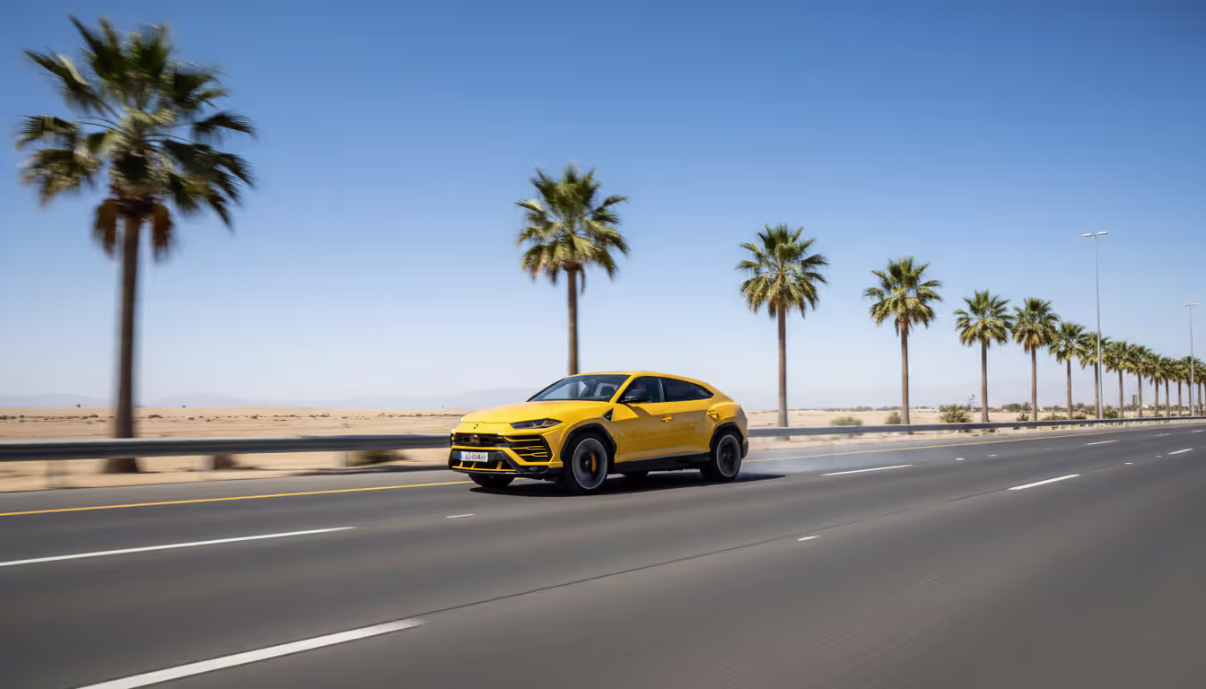 Yellow Lamborghini Urus speeding along a modern desert highway lined with palm trees under a clear blue sky