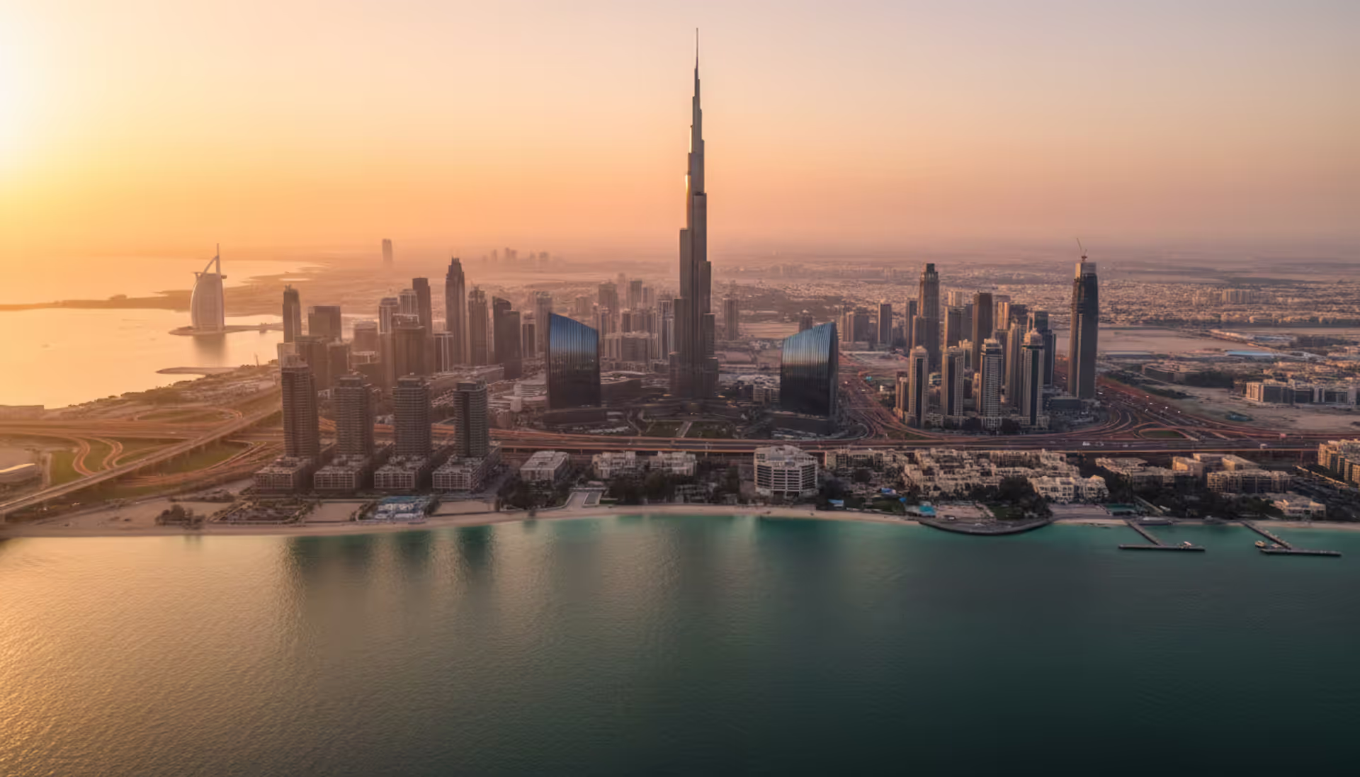 Aerial sunset panorama of Dubai skyline with Burj Khalifa and Burj Al Arab overlooking the turquoise Persian Gulf