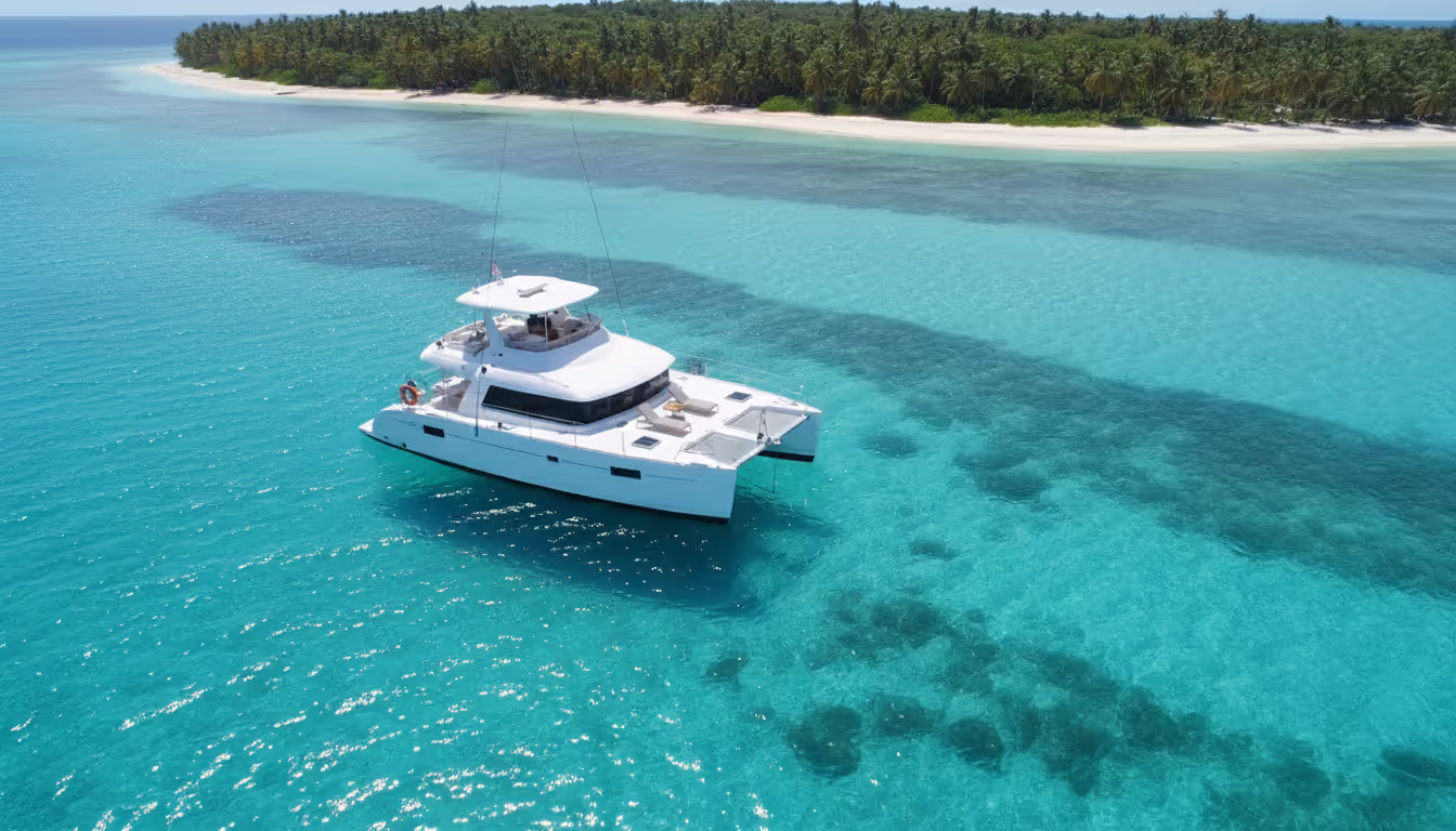 Sunset view from the stern of a luxury yacht in the Caribbean with a dinner table set with wine glasses and the sun setting over calm ocean waters with an island silhouette in the distance