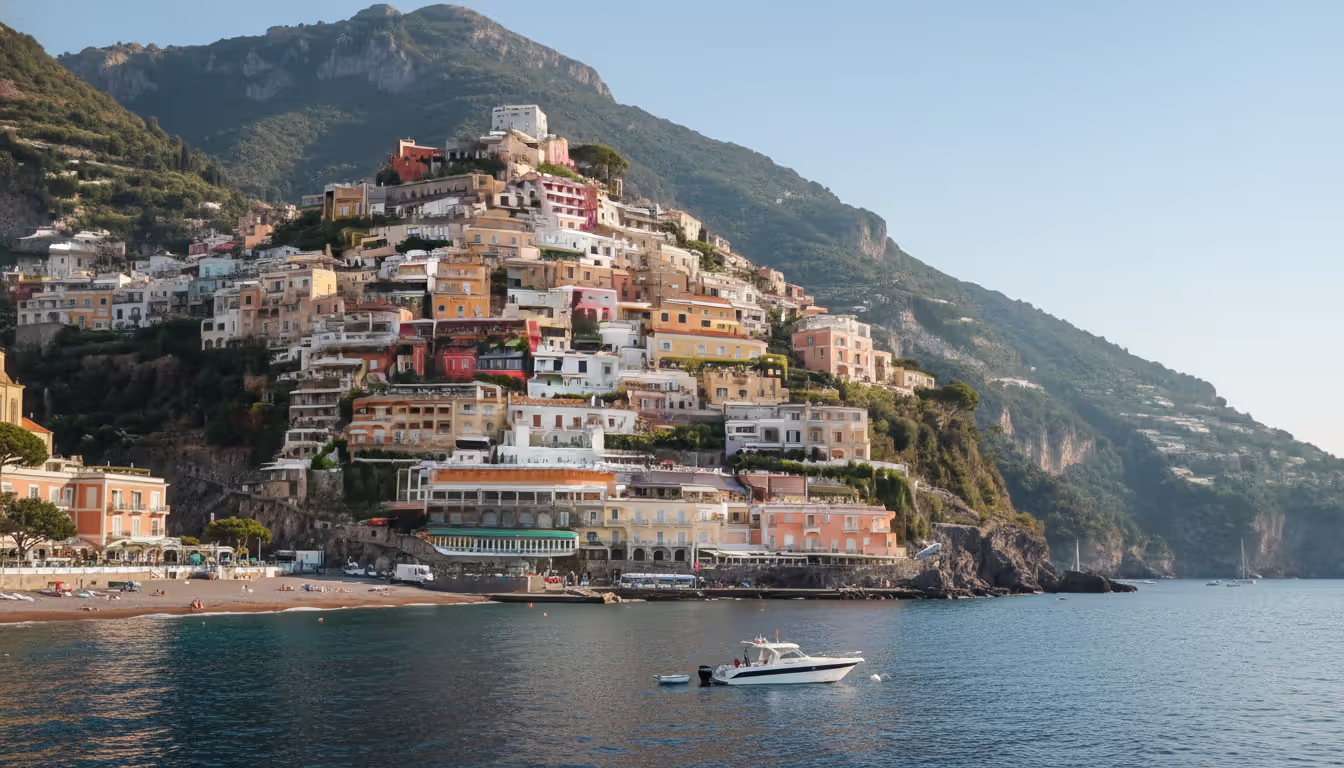 Pastel-colored houses of Positano cascading down steep hillside to the sea with a white yacht anchored offshore on Italy Amalfi Coast